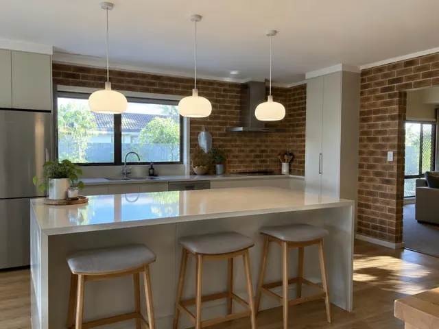 Three white pendant lights above a kitchen island in a brick-walled home interior in Carrara
