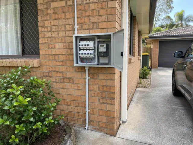 Exterior brick wall with open electrical switchboard and meter beside a driveway in Worongary